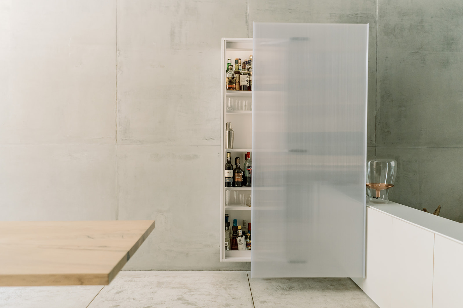 Gabinete bar empotrado con puerta translúcida abierta y botellas en su interior.