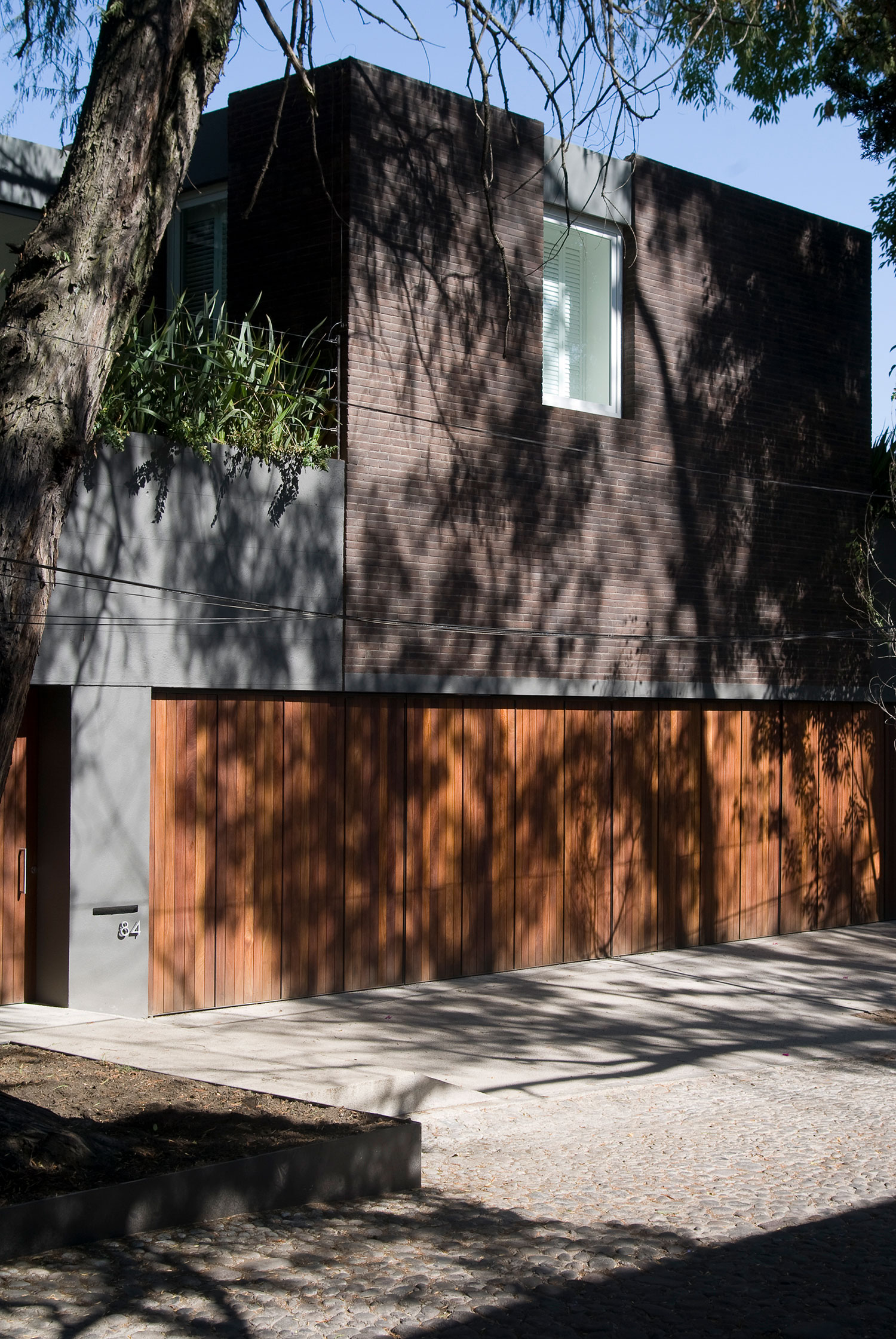 Fachada oscura entre árboles con portón de madera y acceso sombreado.