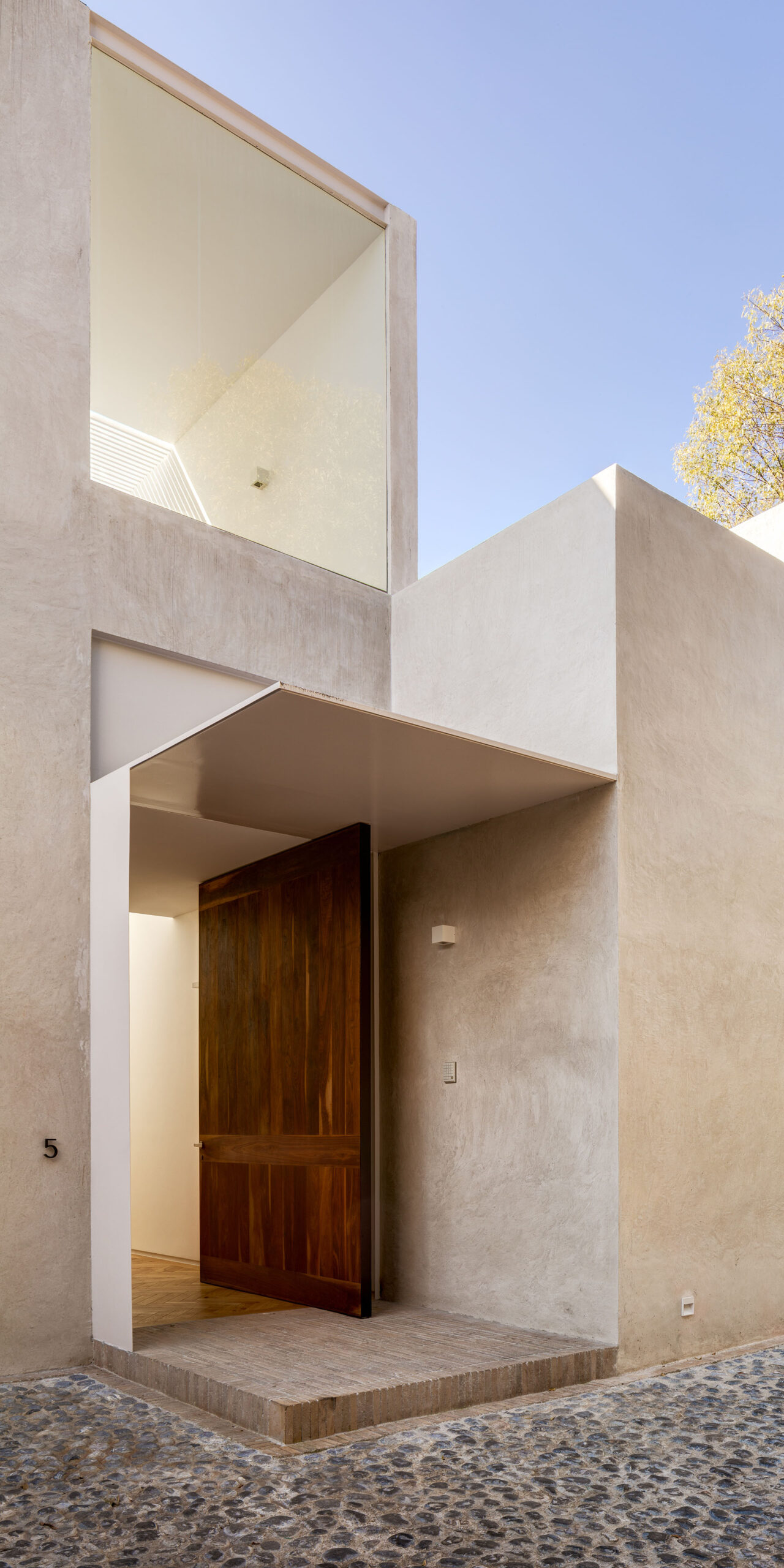 Entrada de madera bajo volúmenes claros y balcones geométricos.