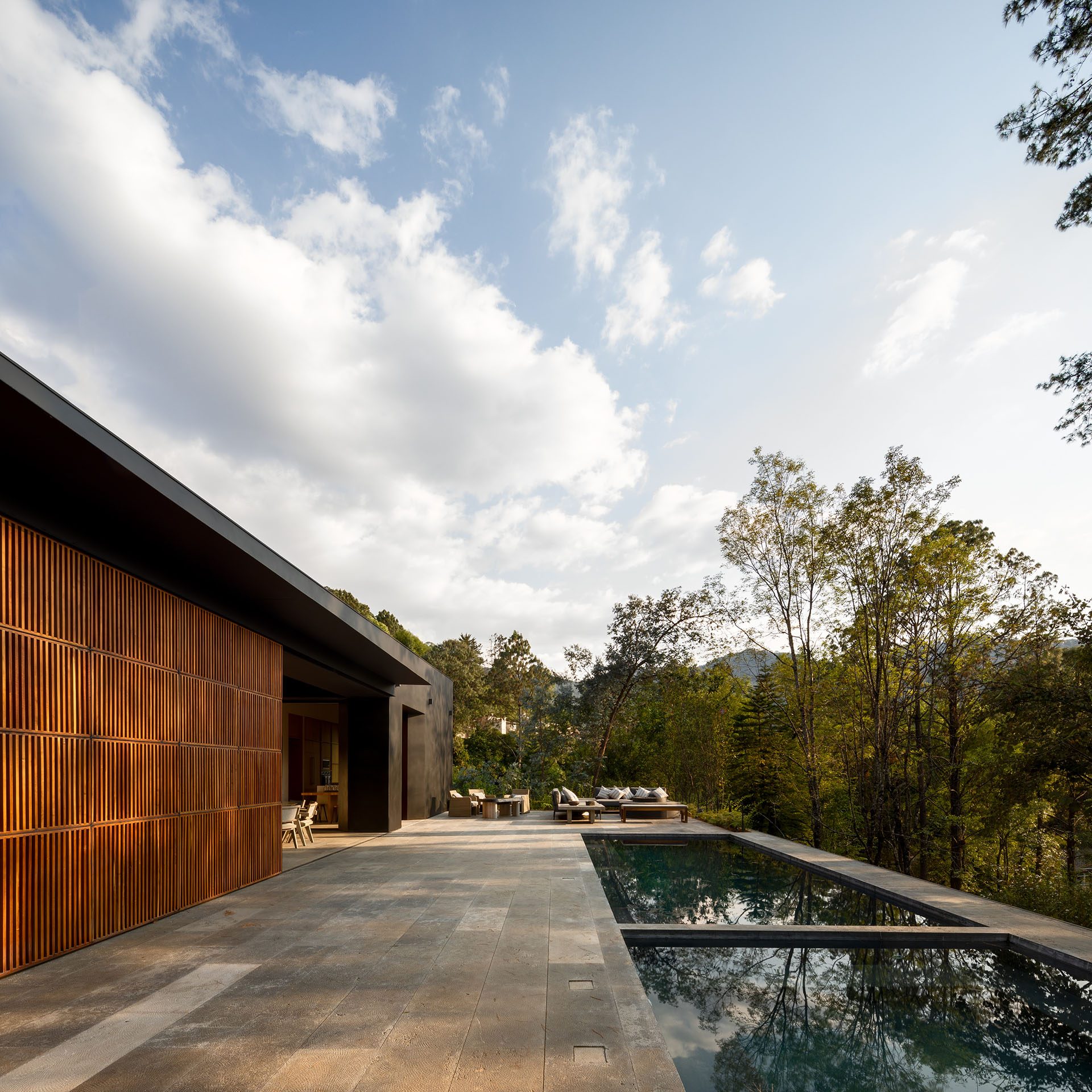 Casa de madera frente a una terraza larga con piscina y bosque.