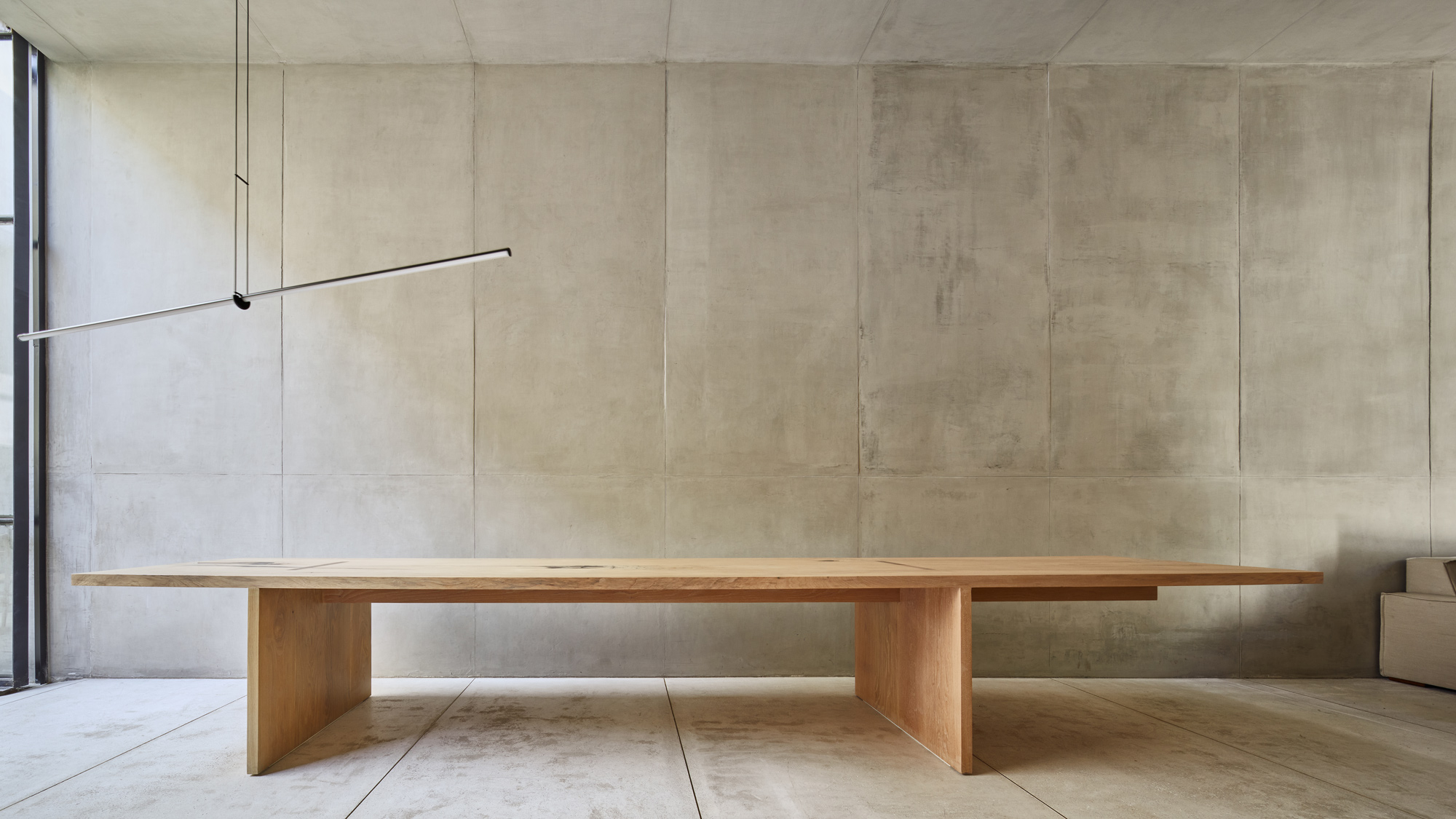 Mesa larga de madera con soportes anchos frente a un muro de concreto.