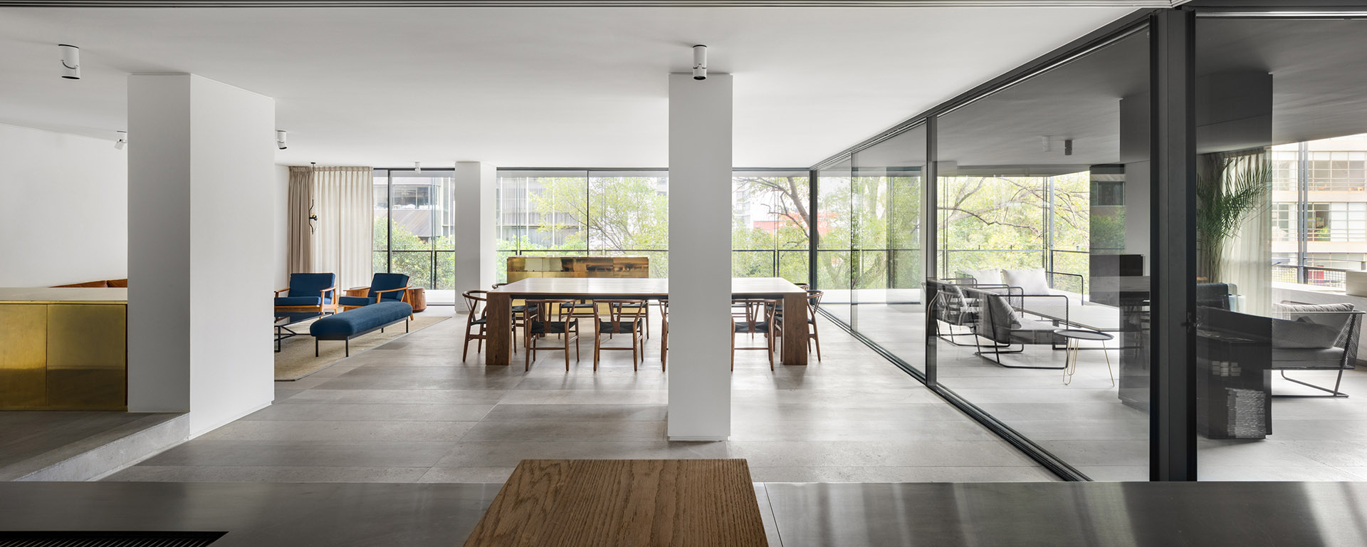Interior abierto con columnas blancas, comedor y cerramientos corredizos de vidrio.