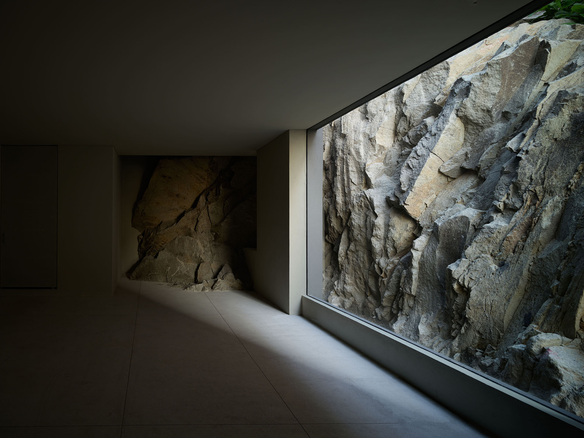 Pasillo oscuro con un gran ventanal que revela un muro natural de roca.