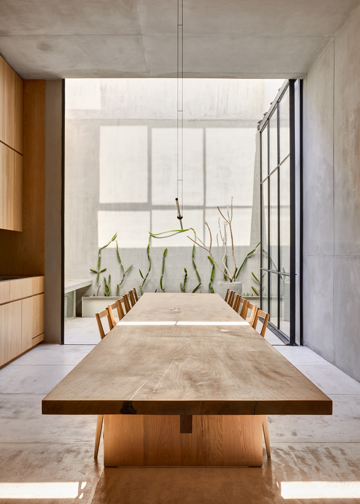 Mesa larga de madera vista de frente en un comedor abierto hacia un patio interior.