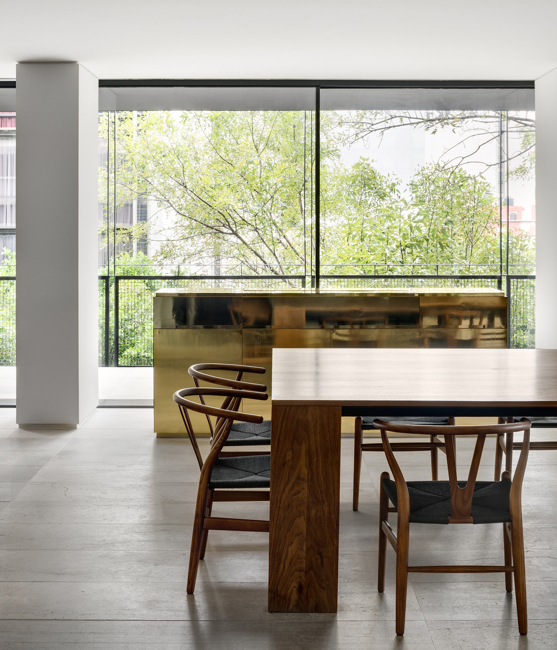 Comedor de madera junto a una cocina abierta y ventanales hacia los árboles.