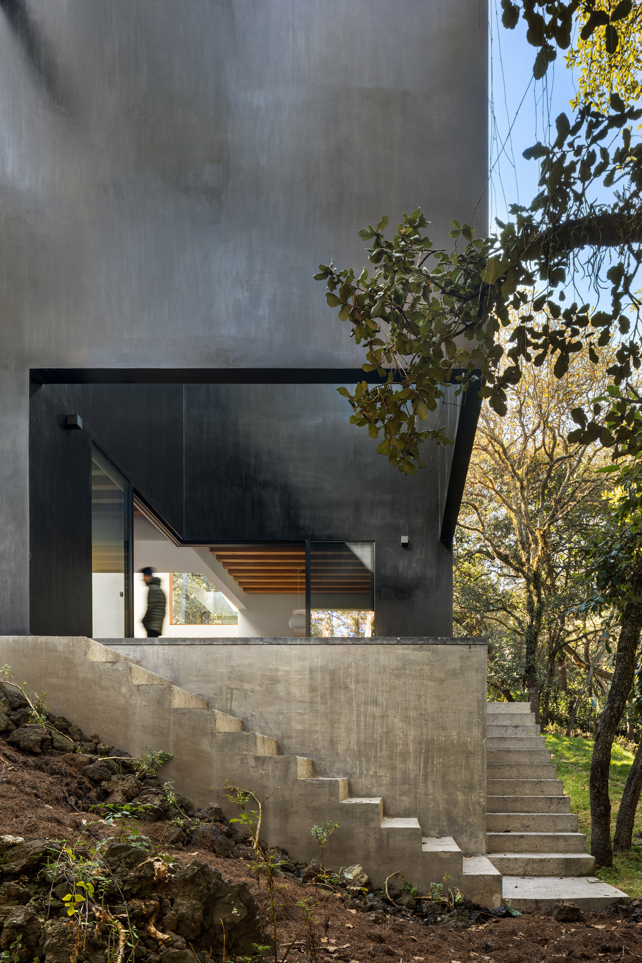 Pabellón oscuro entre árboles, elevado sobre un basamento y escaleras de concreto.