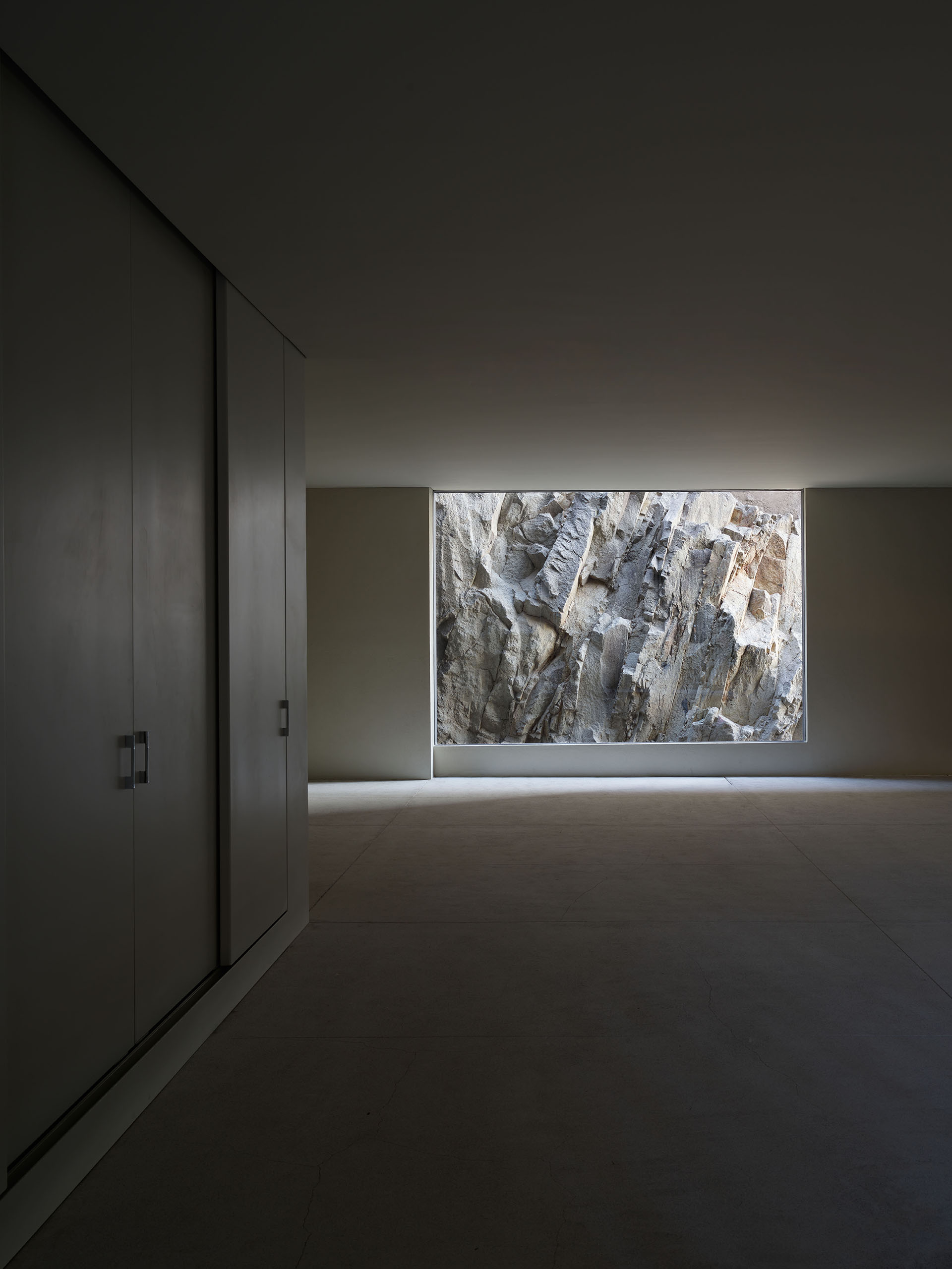 Interior oscuro con armarios y una abertura cuadrada hacia la roca exterior.