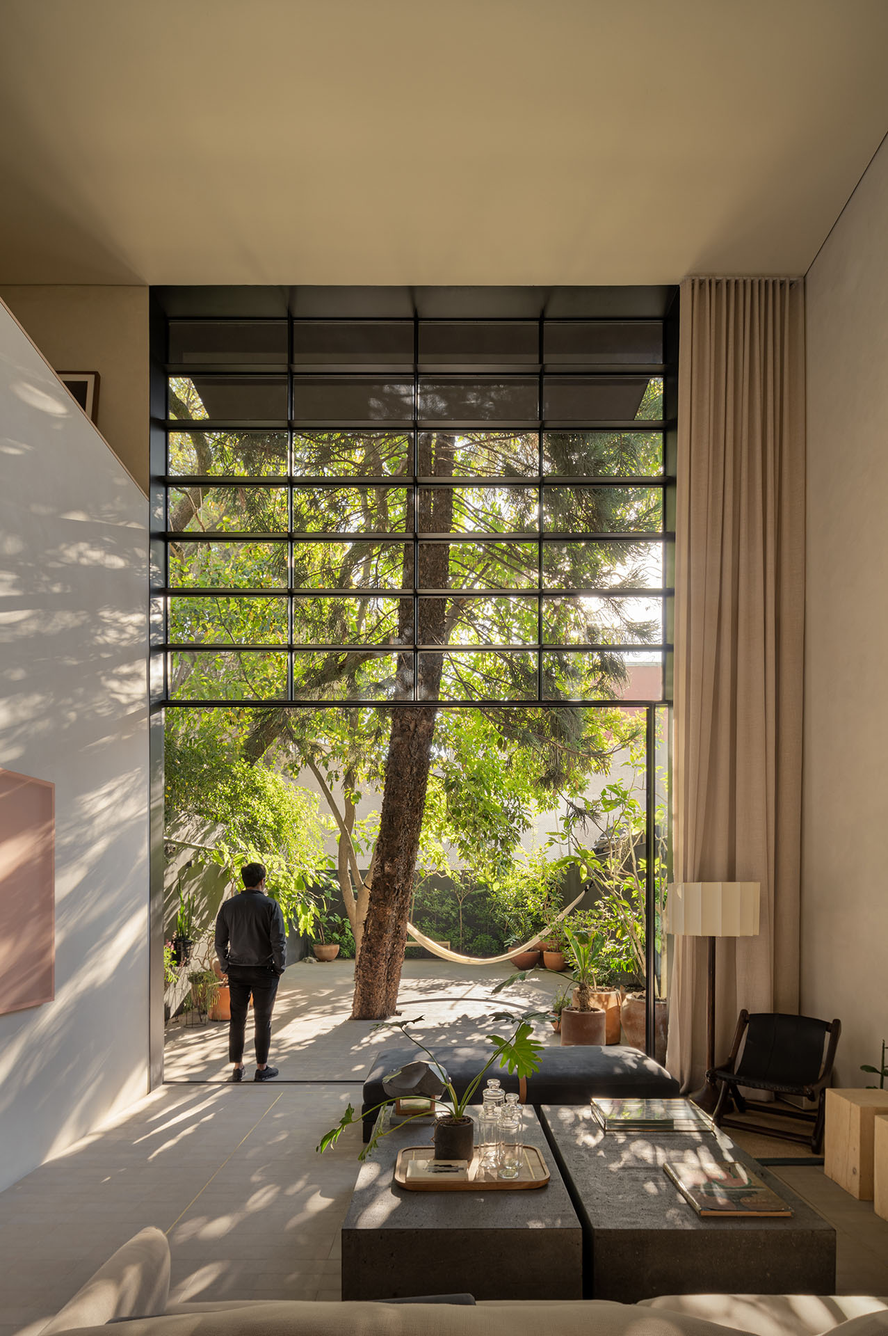 Sala de doble altura abierta al jardín mediante una gran fachada de vidrio.