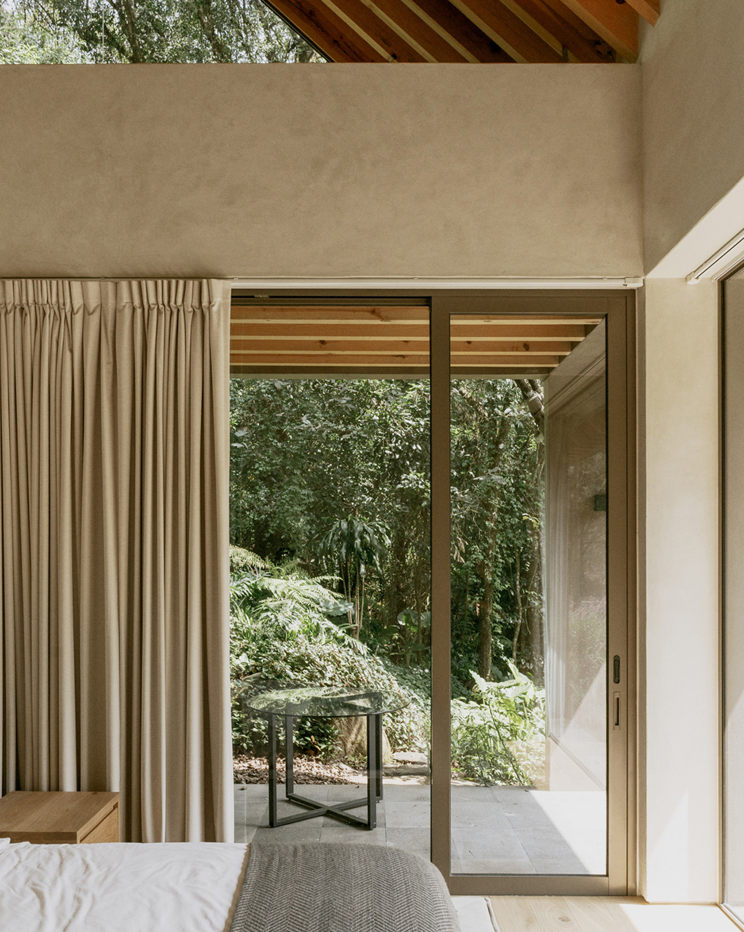 Interior claro con cortinas, puerta corrediza y vista hacia un patio arbolado.